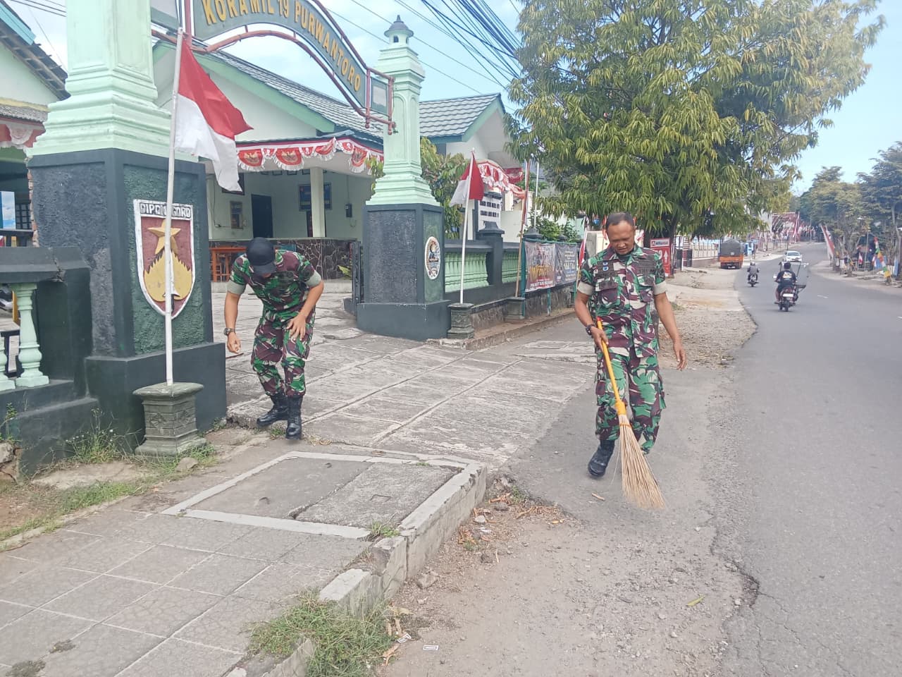 Beberapa prajurit dengan seragam PDL sedang membersihkan dedaunan.